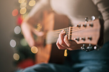 Close up on hand of woman musician playing acoustic guitar at home party at night with bokeh...