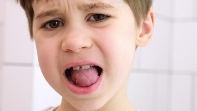 Child shows his loose milk tooth presses and pushes it with his tongue. Open mouth close-up. Caucasian 6 year old kid in a white T-shirt on a bathroom background. lower incisor. Copy space. Body part.