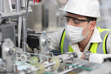 Caucasian mechanic technician maintenance, repairing industrial machinery equipment in factory. Professional worker in protective clothing with goggles and mask using wrench at manufacturing factory