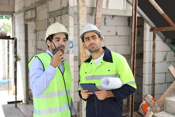 Two technician civil engineer or specialist inspector discussing, brainstorm and planing work with tablet, blueprint and walkie talkie radio together at Industrial building site. Construction concept