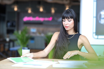 Portrait of confident African businesswoman with happy smiling emotion drinking coffee while sitting and using computer with paperwork on table in restaurant. Success business concept