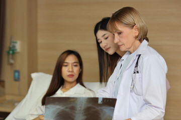 Obraz premium Female doctor greeting and showing happy patient and her friend with x-ray film after surgery in hospital room. Medical and insurance concept.