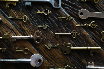 A lot of metal keys and a steel lock on a wooden boards. Vintage rusty padlock surrounded by old...