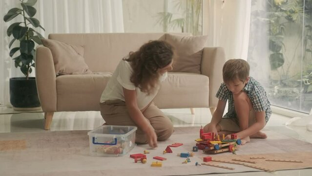 Young mother and pre-teen son playing constructor together on carpet in living room