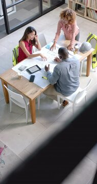 Vertical video of diverse colleagues discussing work over blueprint in office in slow motion