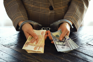 women's handcuffed hands hold dollars on a dark wooden background