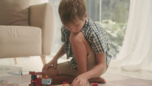 Pre-teen son playing with constructor together with young mother sitting on carpet in living room