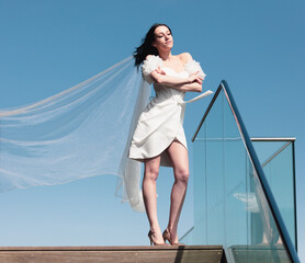 Beautiful brunette woman in a white wedding dress against the blue sky