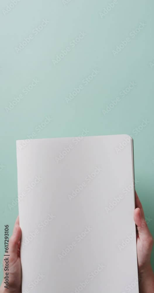 Wall mural Vertical video of hand holding book with copy space on green background in slow motion