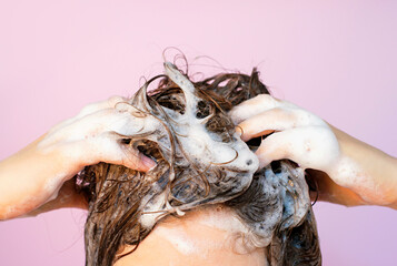 Girl washes her hair with shampoo on lilac background, front view.