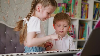 Little girl makes smile on brother face with fingers trying to change mood during music lesson. Sister motivates toddler boy to learn playing piano