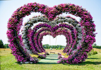 floral wedding arch in shape heart of white and pink petunias in the garden with swing