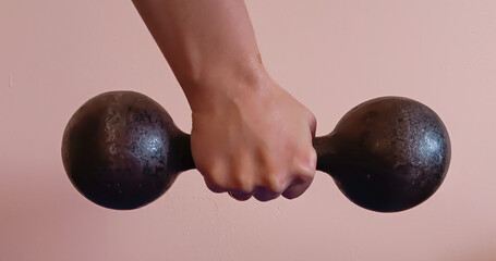 A metal dumbbell created in the Soviet Union in a female hand against a peach-colored wall