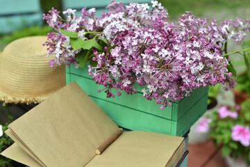 Vintage still life with open book or diary with lilac flowers bouquet and hat in the garden. Summer and spring season concept. Mother's day of Birthday greeting card