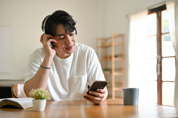 A relaxed Asian man listening to music through his headphones at a table in his living room.