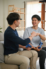 A happy Asian man giving fist bump to his friend while playing video games in the living room