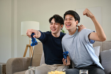 Two overjoyed Asian male friends celebrated their game wins while playing video games together.