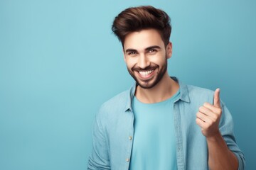 Portrait of handsome young man showing thumbs up gesture on blue background. Generative AI