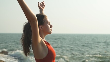 young woman has raised her hands to the sky and is inhaling the scent of the ocean