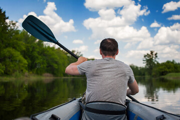male tourist swims in a kayak in the summer along the river against the backdrop of a forest, rear...