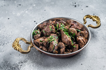 Chicken liver stew with onions and parsley in a skillet. Gray background. Top view
