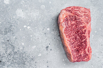 Raw Wagyu striploin or New york steak on a butcher table. Gray background. Top view. Copy space
