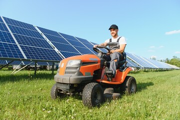 A man drives a lawnmower near solar panels. Concept of solar energy