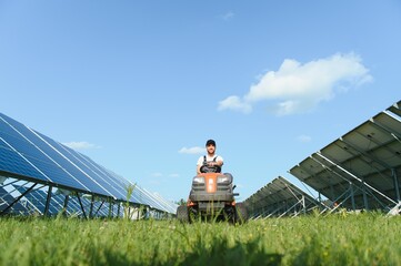 A man working at solar power station. A worker on a garden tractor mows grass on a solar panel farm.