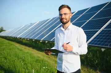 Positive bearded male investor standing against photovoltaic panels producing alternative energy.
