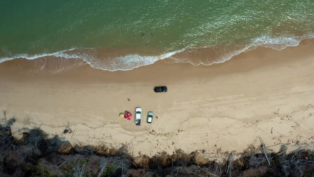 Aerial drone birds eye top view shot following a car drying down the tropical Malemb&aacute; beach with golden sand and calm crystal clear turquoise water near Tibau do Sul in Rio Grande do Norte, Brazil