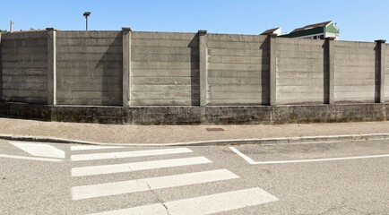 Fototapeta na wymiar Large concrete surrounding wall with sidewalk and crosswalk in front. Background for copy space.