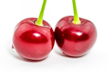 Two fresh vibrant red cherries on green stem closeup.