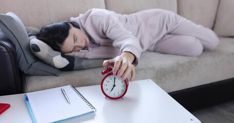 Young woman sleeps couch and turns off ringing alarm clock. Sleep fatigue and depression concept