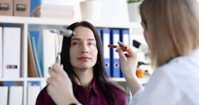 Female doctor checking woman patien eyes with flashlight in medical office. Neurologist or ophthalmologist checking vision concept