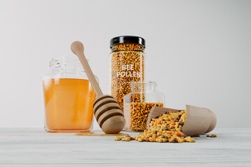 A jar of honey, dipper, wooden scoop and glass pots full of bee pollen granules