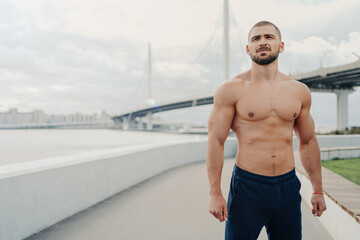 Handsome, muscular man has outdoor fitness workout near river bridge. Sexy body, sporty attire....