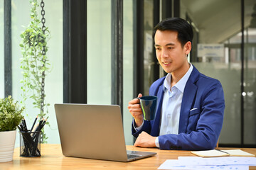 Professional businessman drinking coffee and checking email on laptop at the morning