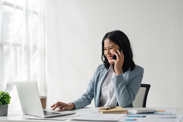 Attractive young business woman talking on the mobile phone and smiling while sitting at her working place in office and at laptop