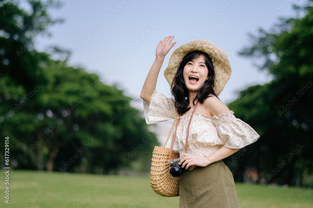 Wall mural portrait of asian young woman traveler with weaving hat and basket and a camera on green public park