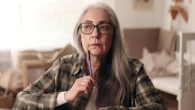 Portrait of gray haired senior woman thinks questioningly and finding solution sitting at desktop at home workplace Idea pointing forward index finger concept