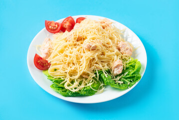 Spaghetti with salmon, cheese and lettuce on a white plate on a blue background.
