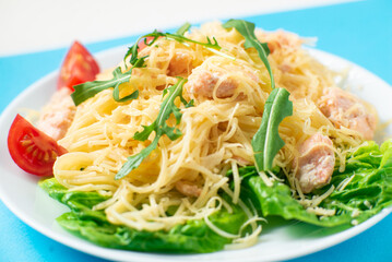 Spaghetti with salmon, cheese on a lettuce salad sprinkled with arugula and cherry tomatoes close-up.