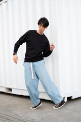 Portrait of stylish handsome asian model wearing black casual hoodie and jeans, posing near the wall on the street, urban lifestyle 