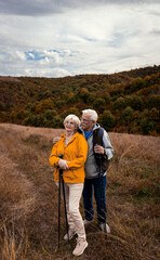 Active senior couple with backpacks hiking together in nature on autumn day..
