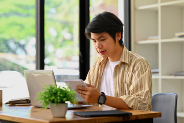 Millennial asian businessman sitting at office desk checking schedule or handwriting important information