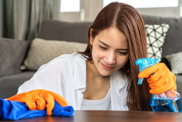 Young asian woman in protective gloves using disinfectant spray and while cleaning and washing...