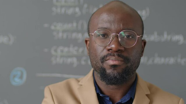 Close up portrait of male African American teacher standing in front of blackboard looking at camera and smiling in programming classroom at daytime