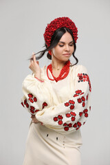 Vyshyvanka day in Ukraine. Beautiful young brunette woman dressed in Ukrainian traditional ethnic embroidered shirt, vyshyvanka, red wreath and necklaces at studio. Independence day, folk concept.