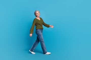 Full length photo of satisfied pleasant good mood woman dressed khaki sweater walk to empty space isolated on blue color background