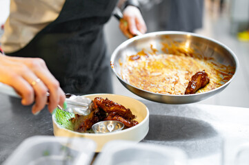 woman chef cooking chicken wings in a sauce in the kitchen